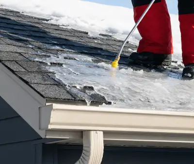 Ice dam removal technician using a steam wand to melt thick ice buildup on a residential roof in Fargo, ND