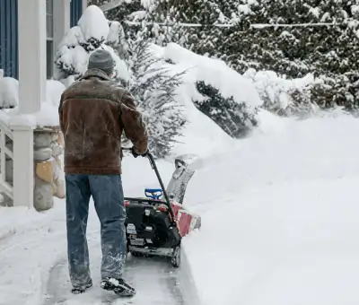 Residential snow removal technician using a snow blower to clear a home driveway and walkway in Fargo, ND
